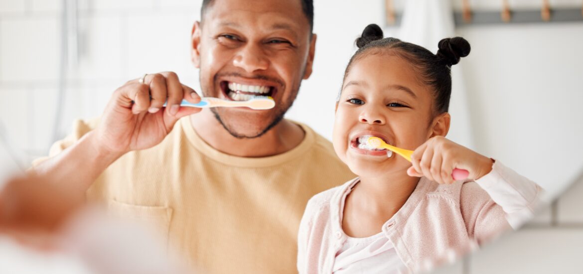 father and daughter brushing their teeth in front of a mirror