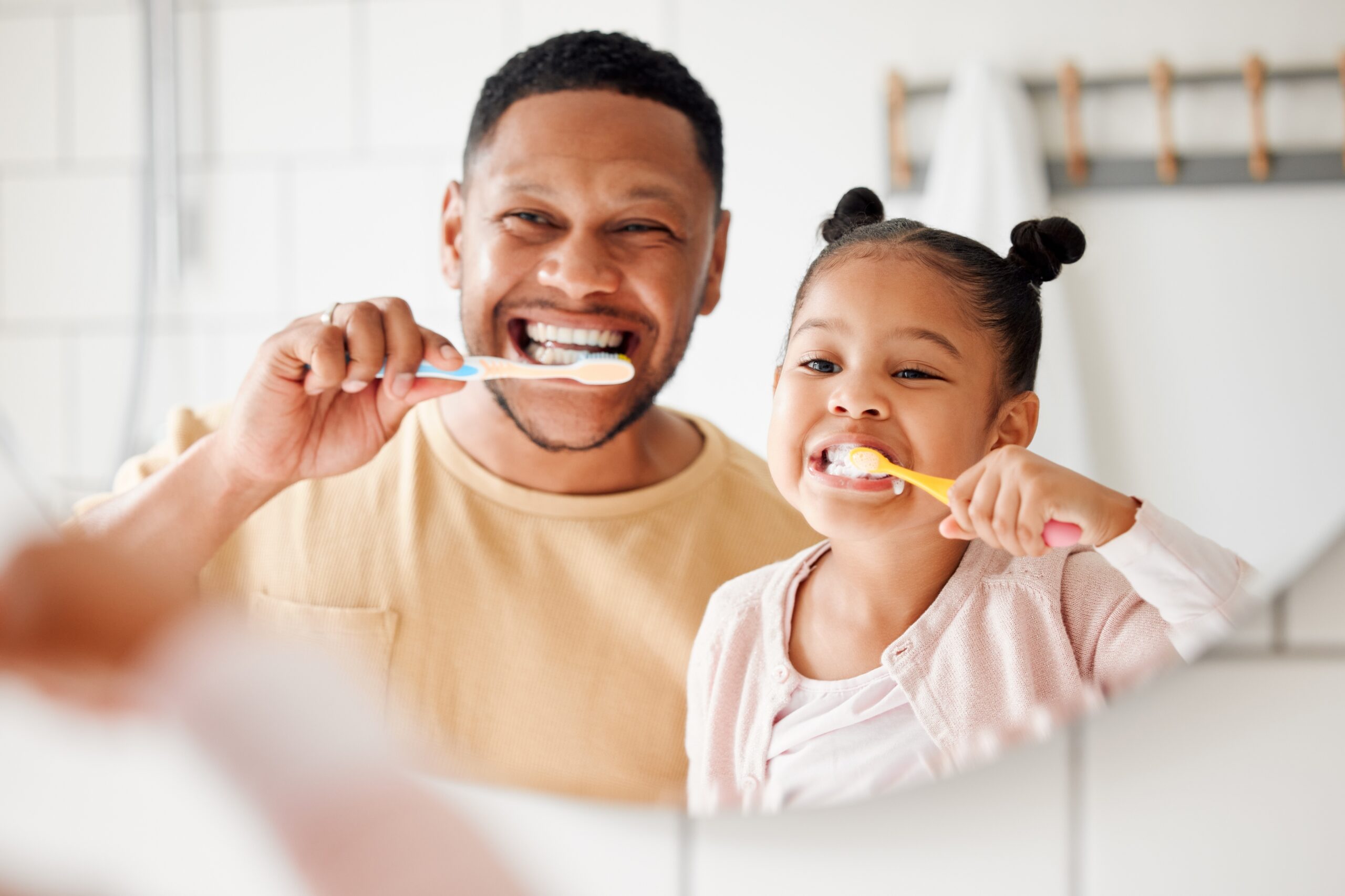 father and daughter brushing their teeth in front of a mirror