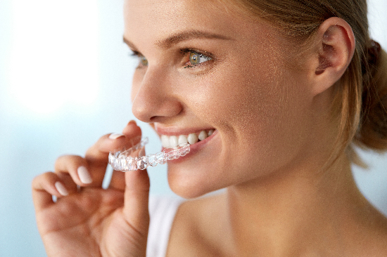 young woman smiling, placing her Invisalign in her mouth