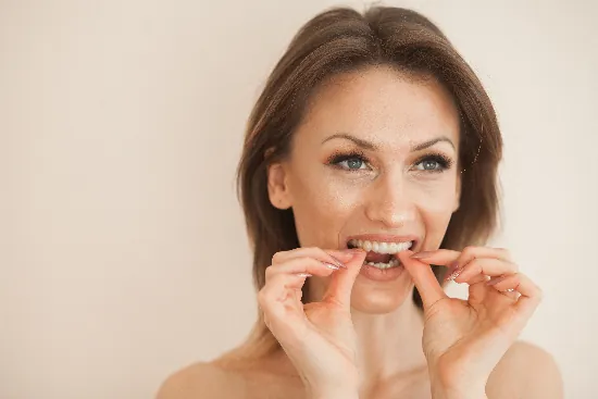 woman putting in her clear aligner against a beige background