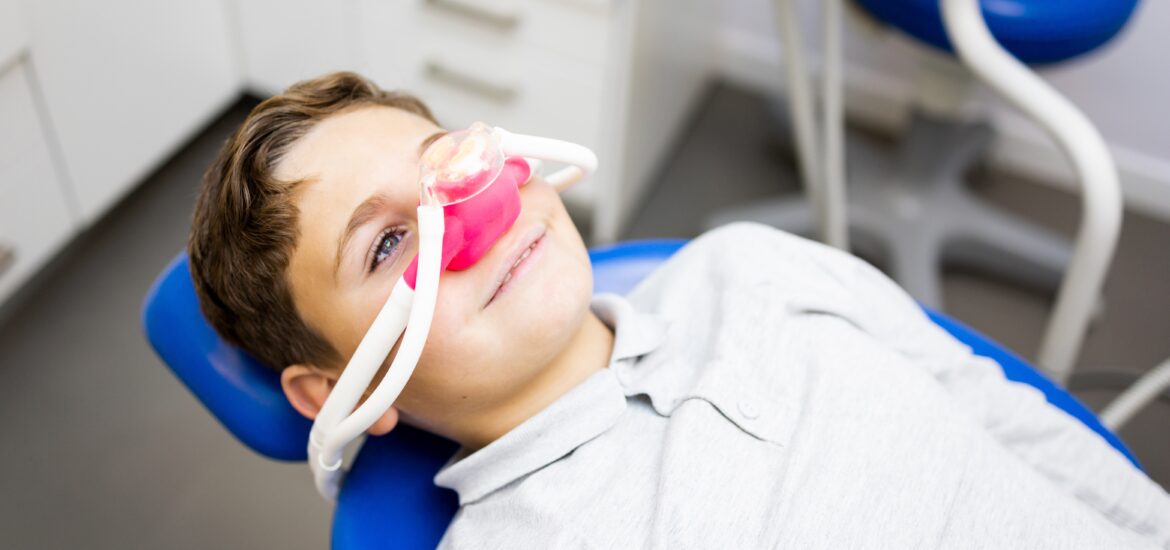 A little boy sits in a dentist's office wearing a nasal mask to breathe nitrous oxide to relax.