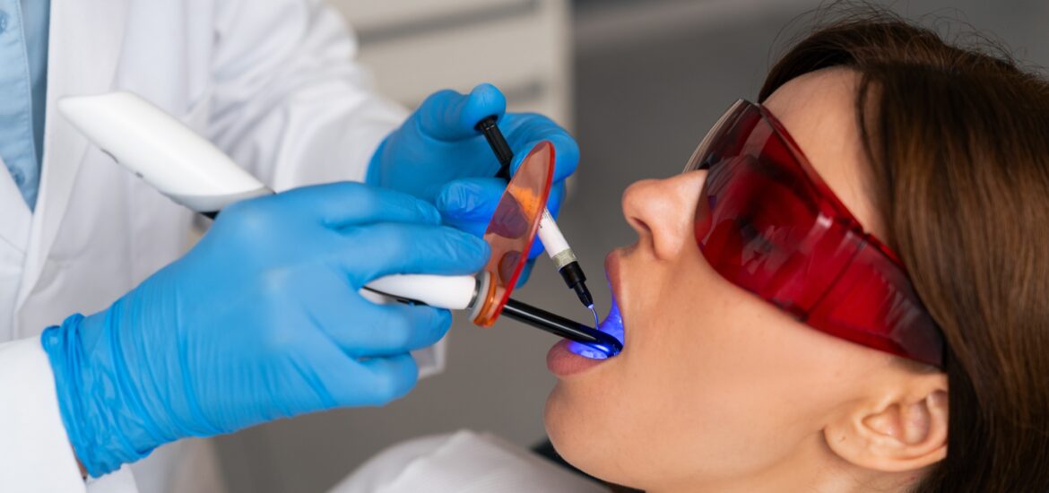dentist in blue gloves treating a woman's gums with laser