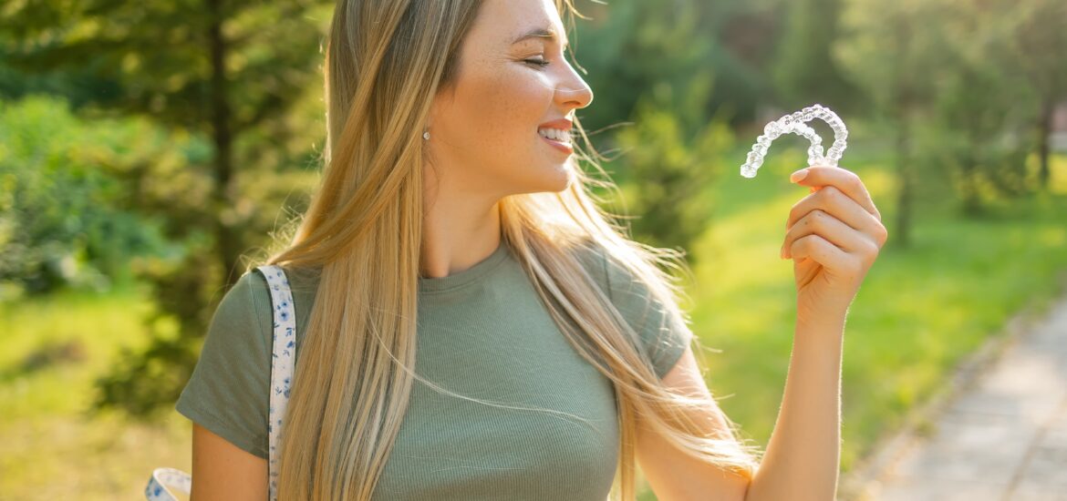 side view of a young woman outdoors, holding up clear aligners