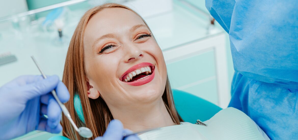 Attractive young woman with naturally white teeth in a dental clinic. Dental doctor's hands with medical tools
